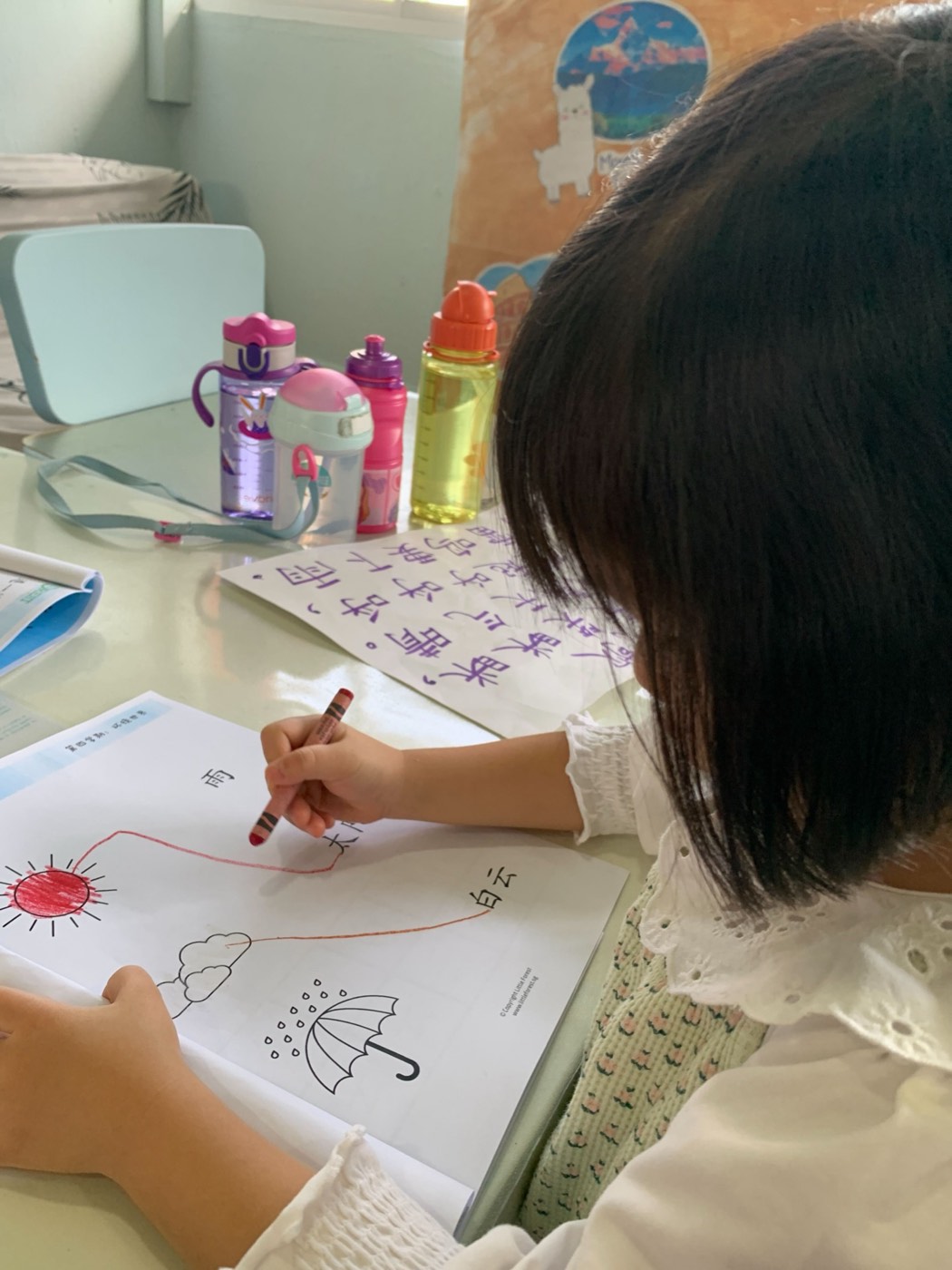 A young girl seen from behind, colouring her own bilingual worksheet at a Little Forest table